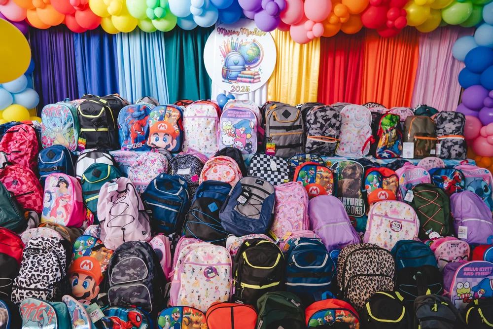Hundreds of packed backpacks lined up in front of a rainbow balloon arch