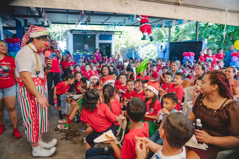 A clown entertains children and families under a festive canopy